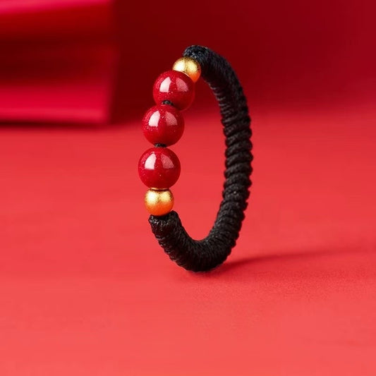 Cinnabar Cord Ring – Black braided cord ring with three red cinnabar beads and gold spacers on red background