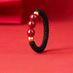 Cinnabar Cord Ring – Black braided cord ring with three red cinnabar beads and gold spacers on red background