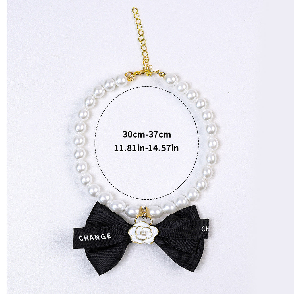Luxury Crystal Pet Necklace – pearl collar with black bow and white enamel camellia charm, gold hardware, flat lay