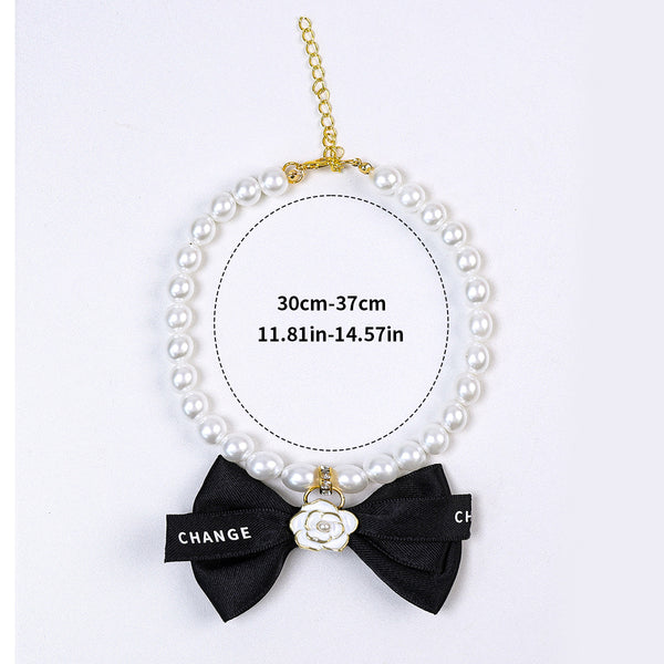 Luxury Crystal Pet Necklace – pearl collar with black bow and white enamel camellia charm, gold hardware, flat lay