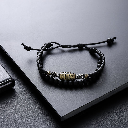 Dzi Bead Bracelet – black woven cord with gold central bead and matte black beads, adjustable knot on dark leather