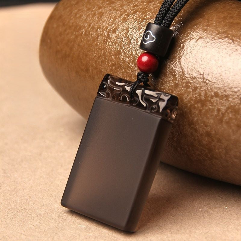 Black Obsidian Pendant – Icy black obsidian plaque with cloud pattern and red bead near ceramic pot, balance stone