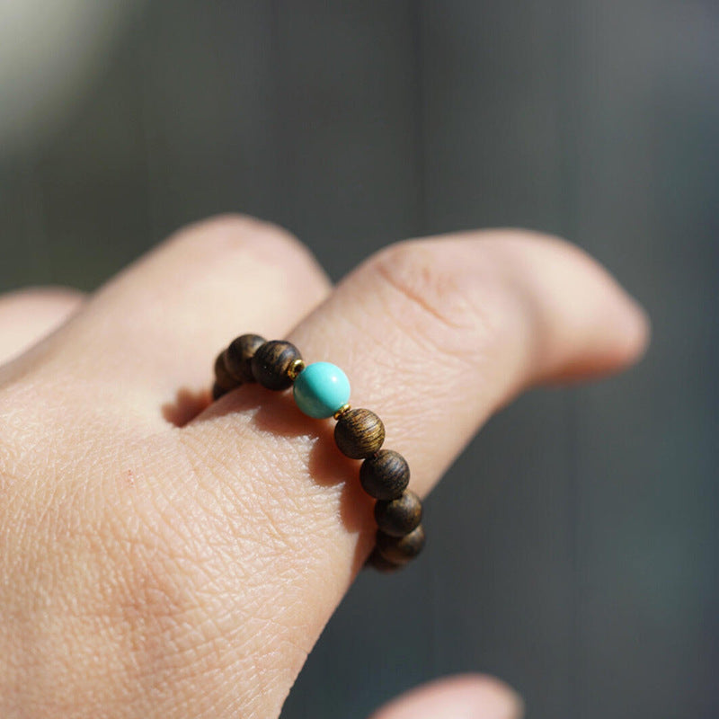 Agarwood Ring – brown wood beads with turquoise accent bead on finger, natural sunlight, calming accessory
