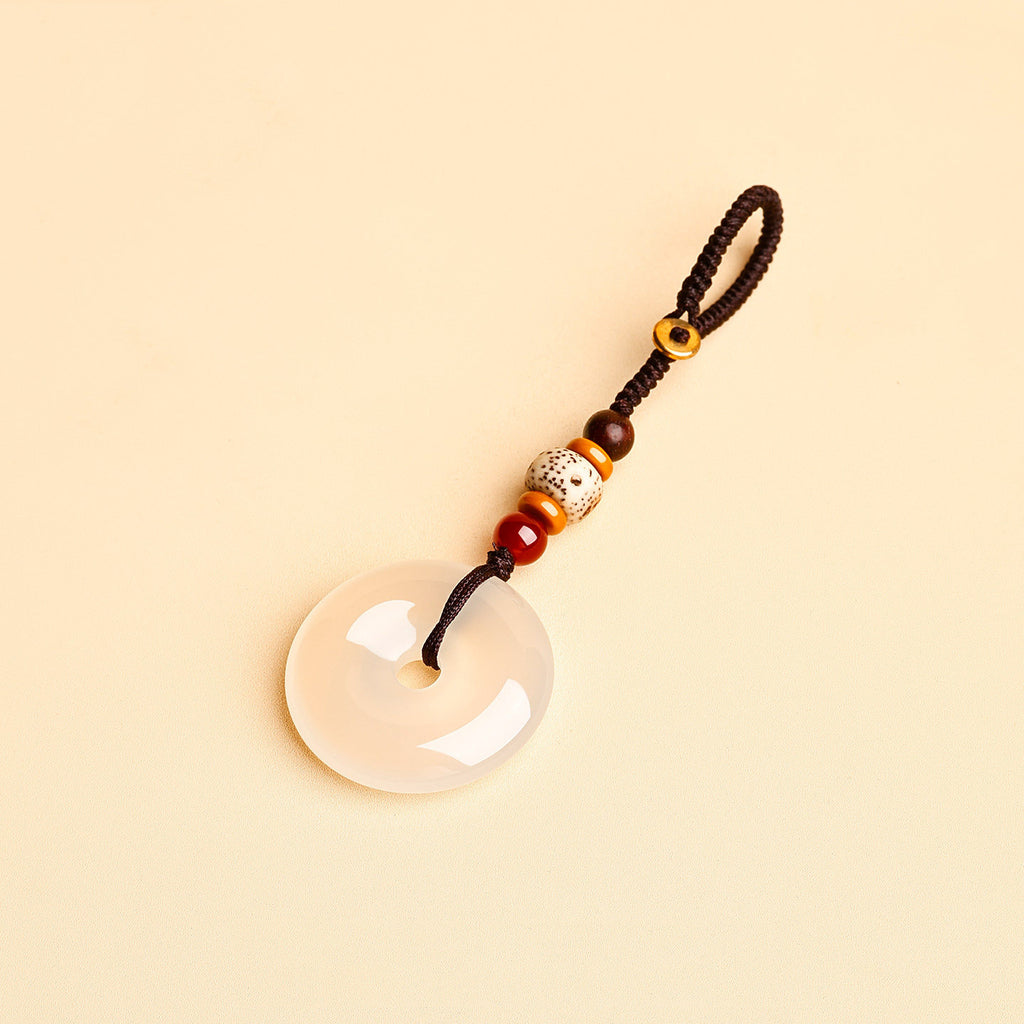 Jade Keychain Pendant – White jade donut pendant with braided rope and bodhi beads on beige background, feng shui