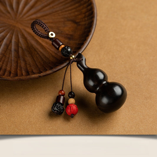 Sandalwood Gourd Keychain – dark ebony gourd with red and black accent beads on tan surface