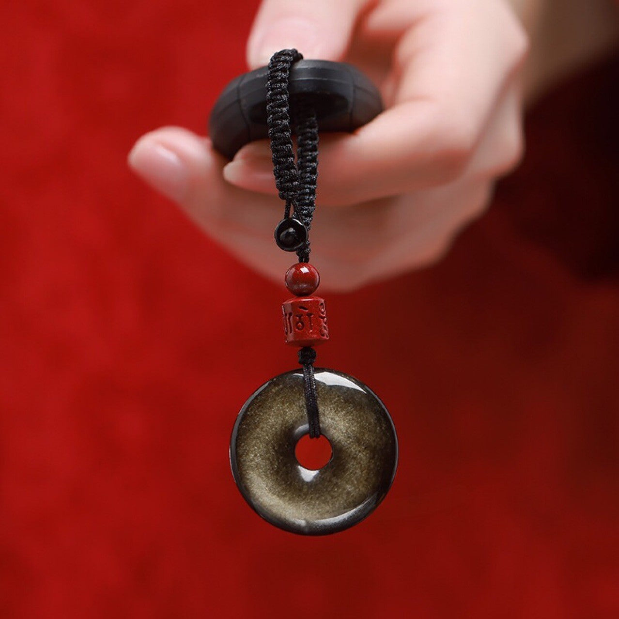 Gold Obsidian Pendant – Hand holding gold sheen obsidian keychain with red bead against red background, protection charm