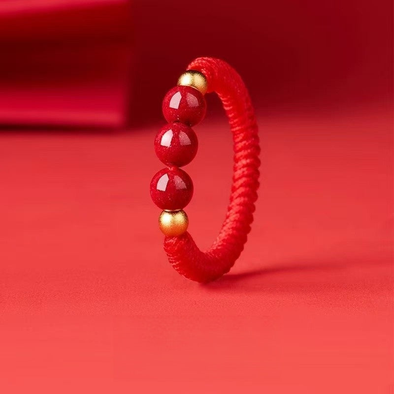 Cinnabar Cord Ring – Red braided cord ring with three red cinnabar beads and gold accents on red background
