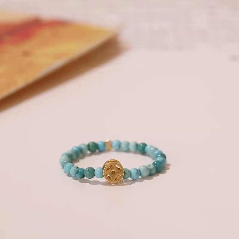 Turquoise Coin Ring – Turquoise bead ring with gold Chinese coin charm on light background, wealth feng shui ring