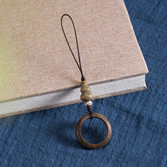 Sandalwood Phone Grip – Light wood ring lanyard with white spotted bead on book over blue fabric, natural wood phone charm