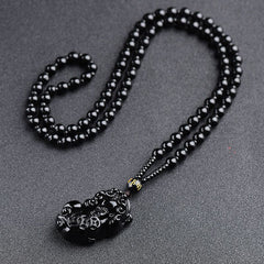 Obsidian Pixiu Necklace – Black obsidian bead chain with carved pixiu pendant on gray, protection amulet