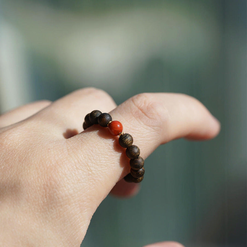 Agarwood Ring – wooden bead ring with red coral center stone, outdoor greenery background, zen style