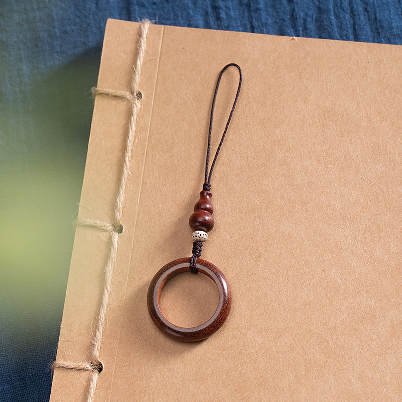 Sandalwood Phone Grip – Dark reddish brown wood ring grip with white bead on traditional bound book, vintage phone lanyard