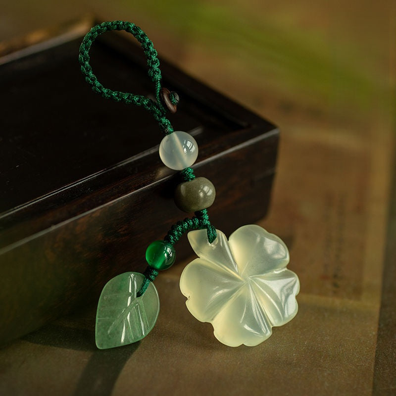 Jade Clover Keychain – clover with woven green loop and leaf charm resting on dark wood Imagen principal del producto