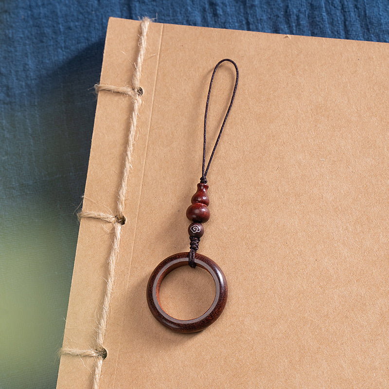 Sandalwood Phone Grip – Deep red wood ring lanyard with carved accent bead on kraft paper book, elegant phone holder