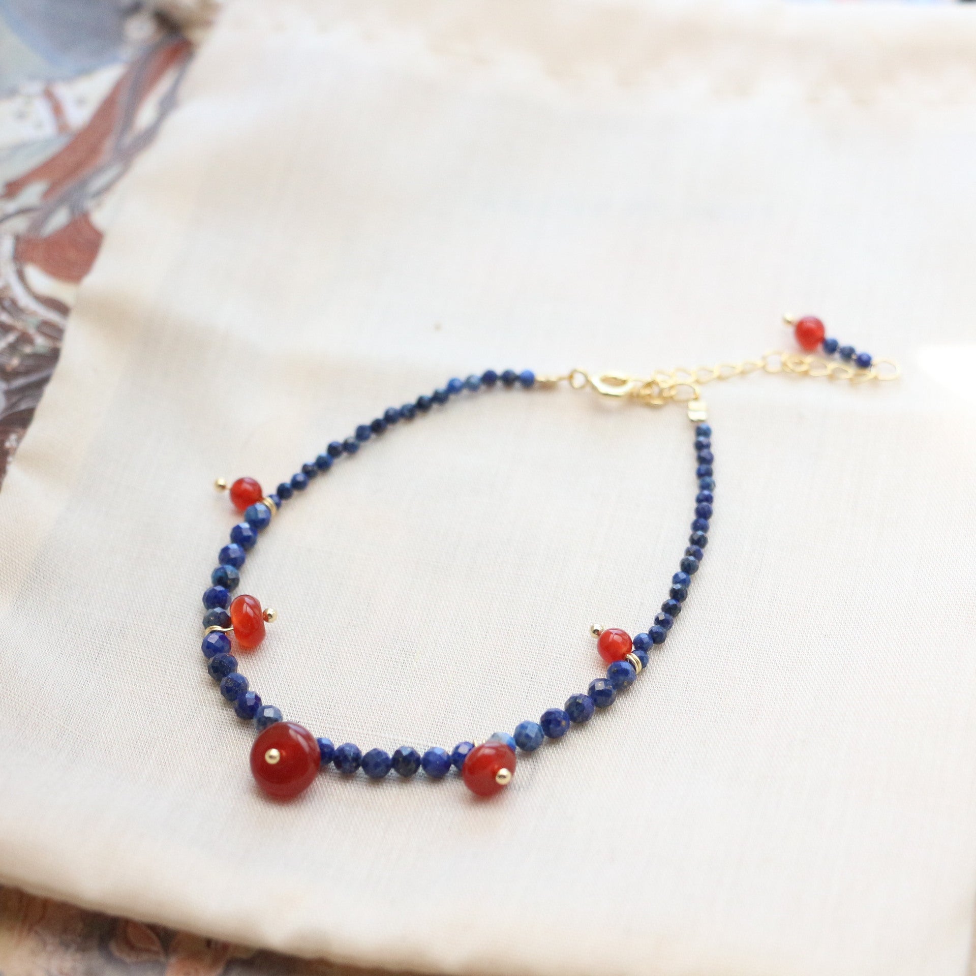 Lapis Lazuli Agate Bracelet – blue lapis lazuli beads with red agate rounds and gold chain clasp on cream fabric, spiritual balance jewelry