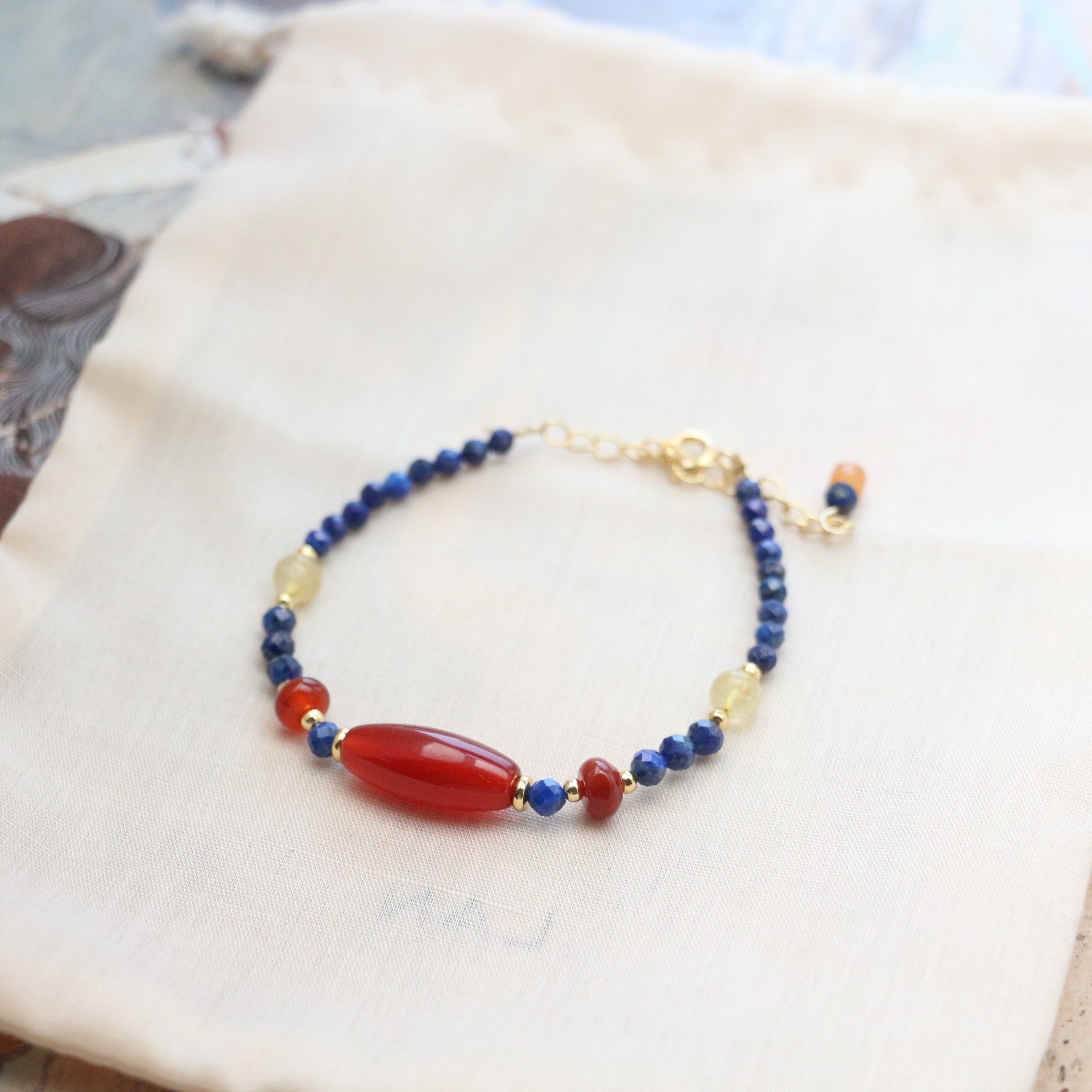 Lapis Lazuli Agate Bracelet – blue lapis strand with large red agate barrel and pale yellow crystal, gold extender chain, fabric background
