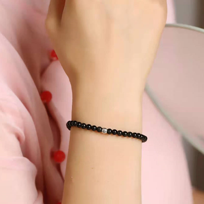 Black Obsidian Smoky Quartz Bracelet – Black beads with silver accent worn on wrist against soft pink fabric with red floral details, side angle shallow depth of field