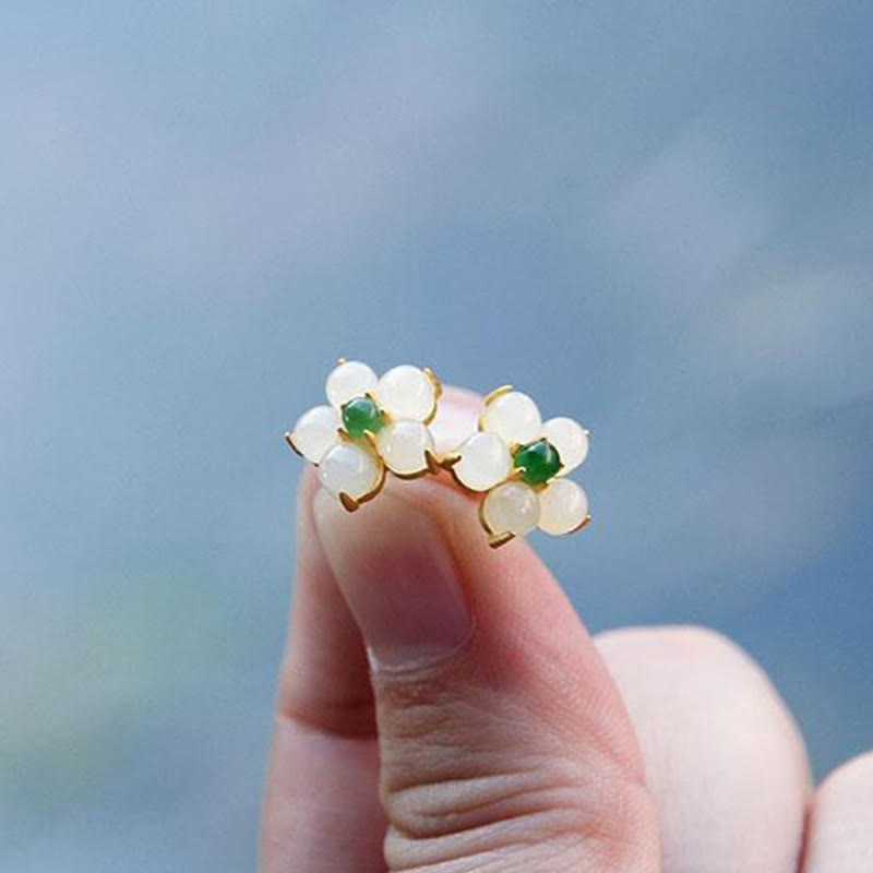 White Jade Flower Blessing Stud Earrings – White jade flower stud earrings with green center stones in gold frames, blue-gray soft gradient sky background, low macro angle