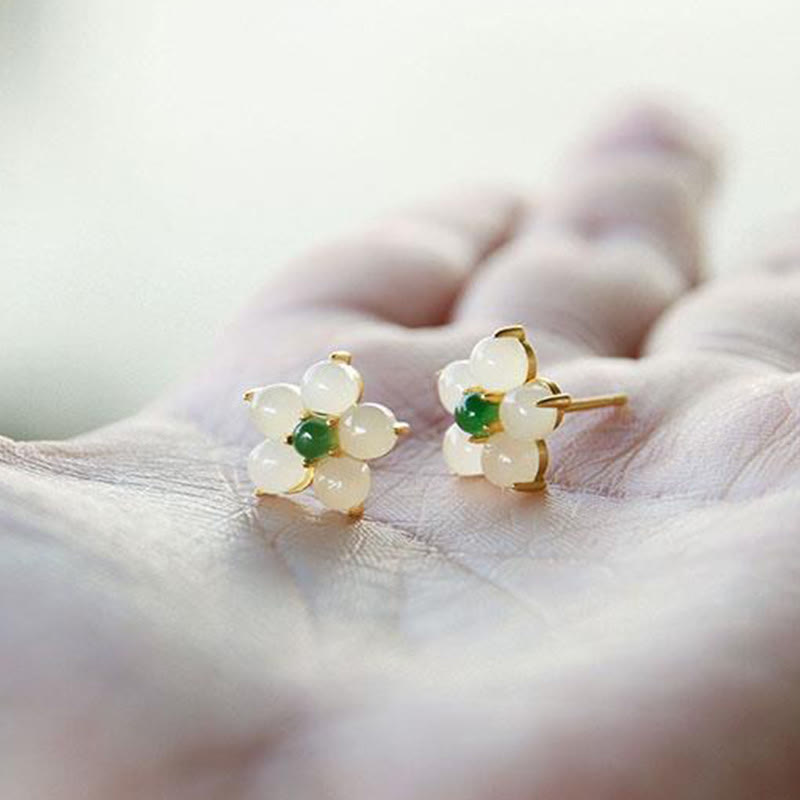 White Jade Flower Blessing Stud Earrings – White jade petal flower studs with green jade centers and gold butterfly backs on open palm, natural soft lighting side angle