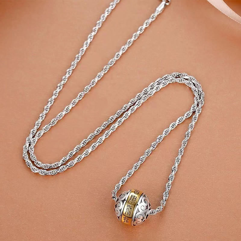 Taoist Nine-Character Mantra Copper Pendant – Silver rope chain with gold-character rotating bead pendant, smooth beige tan surface top-down angled view