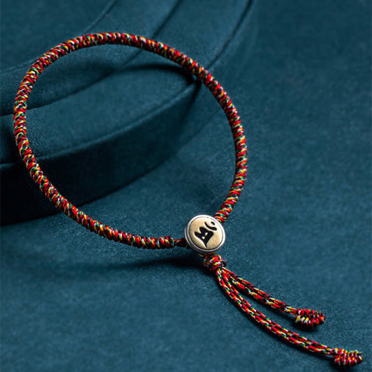 Chinese Zodiac Natal Buddha Bracelet – Multicolor braided cord with gold Sanskrit bead on dark teal fabric, spiritual healing bracelet