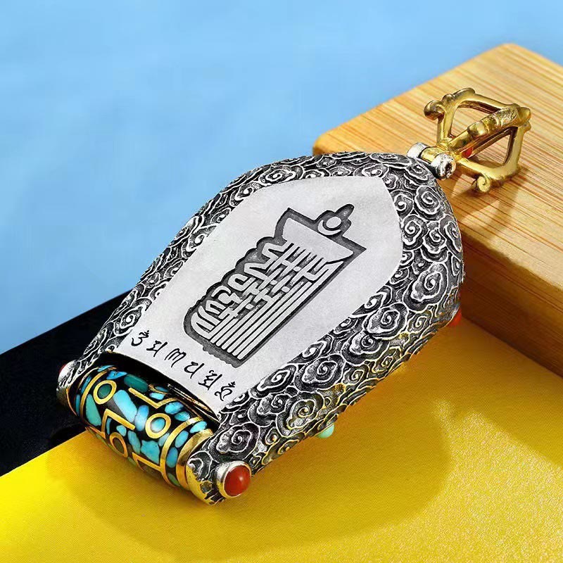 Tibetan Zodiac Buddha Dzi Bead Necklace – Gold Tathagata Buddha figure encased in ornate silver frame with turquoise coral stones and prayer wheel, warm tan wooden surface