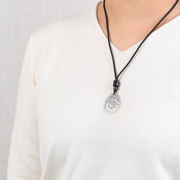Yin Yang Bagua Water Drop Necklace – Silver teardrop pendant with embossed circular pattern and spiral design on black cord worn with white V-neck, gray background