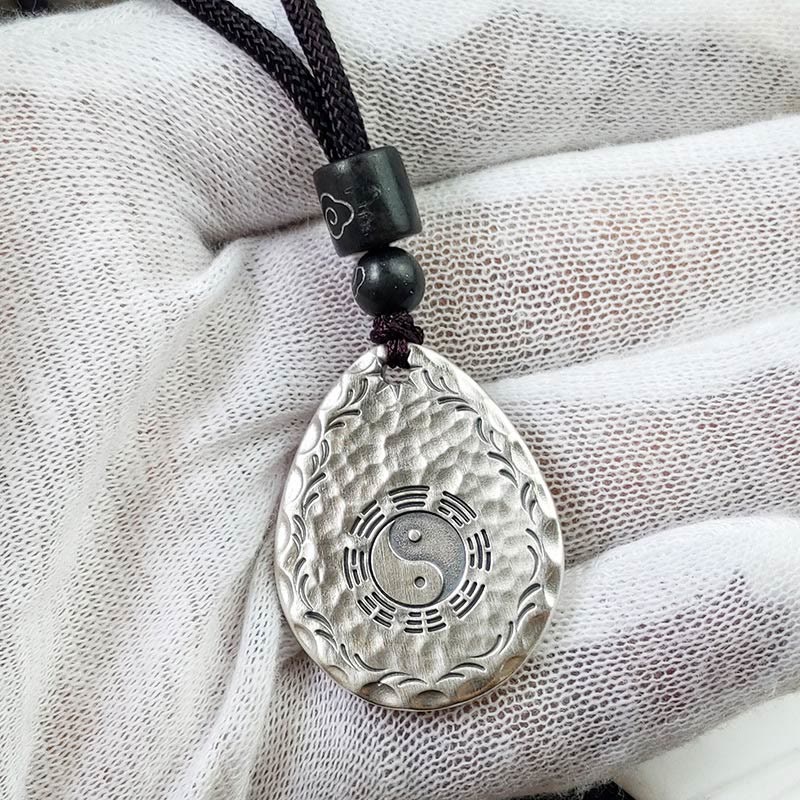Yin Yang Bagua Water Drop Necklace – Silver teardrop yin-yang bagua pendant with wave border on black cord with dark beads, white textured fabric elevated front