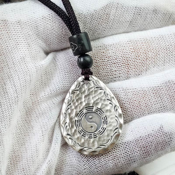Yin Yang Bagua Water Drop Necklace – Silver teardrop yin-yang bagua pendant with wave border on black cord with dark beads, white textured fabric elevated front