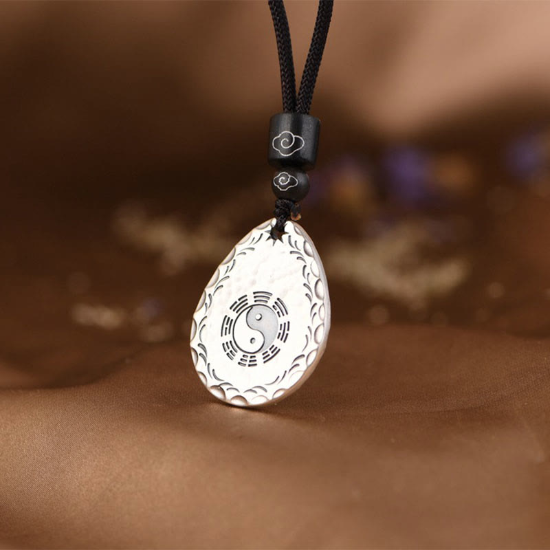 Yin Yang Bagua Water Drop Necklace – Silver teardrop pendant with yin-yang and bagua trigrams, wave-pattern border on black cord with cloud-motif beads, brown fabric