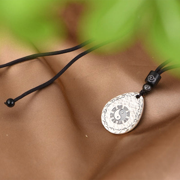 Yin Yang Bagua Water Drop Necklace – Silver teardrop pendant with yin-yang and bagua worn on collarbone with black cord and cloud beads, green foliage lifestyle