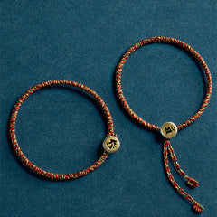Chinese Zodiac Natal Buddha Bracelet – Two red green gold cord bracelets with engraved zodiac charms, top-down flat lay on teal background