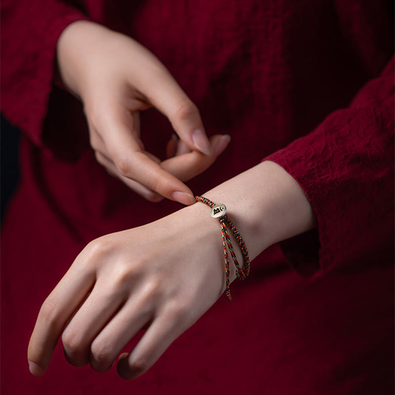 Chinese Zodiac Natal Buddha Bracelet – Multicolor cord bracelet with gold zodiac charm worn on wrist, burgundy fabric lifestyle shot
