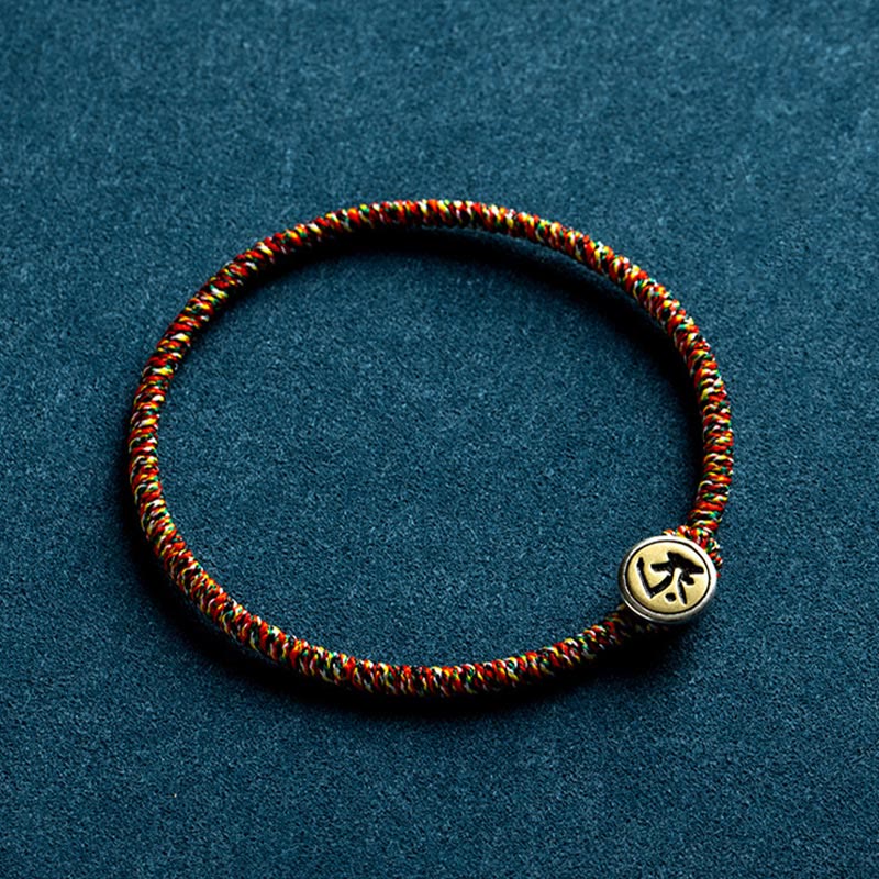 Chinese Zodiac Natal Buddha Bracelet – Red green gold braided cord with gold-toned Chinese character bead, teal fabric flat lay view