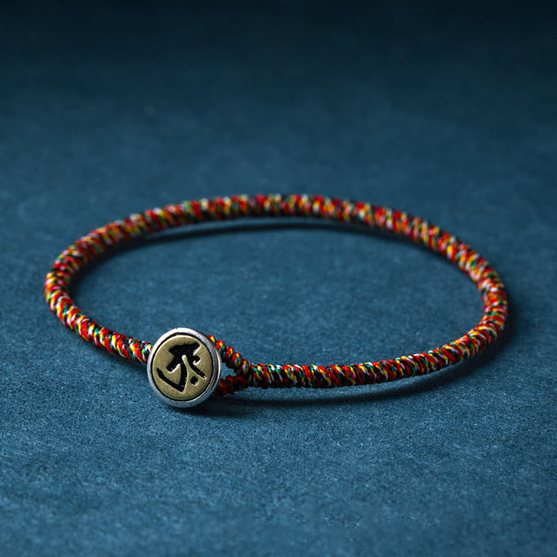 Chinese Zodiac Natal Buddha Bracelet – Multicolor braided cord with brass engraved charm, elevated side angle on dark blue fabric